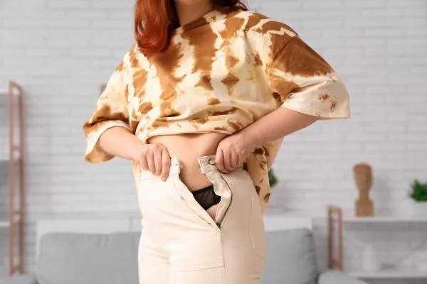 Image of woman trying to do her trousers up after pregnancy weight gain Newham