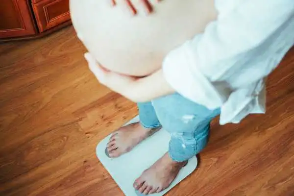Image of woman weighing herself and experiencing weight gain through pregnancy Newham